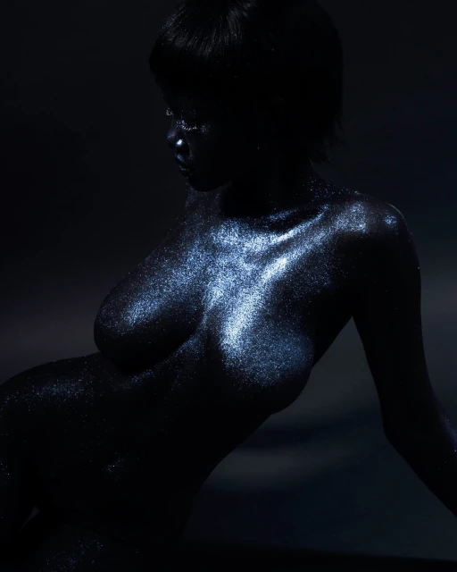 Shimmering nude adult female body covered in glitter, reclining pose, low key lighting, dark background, beauty and fashion editorial.