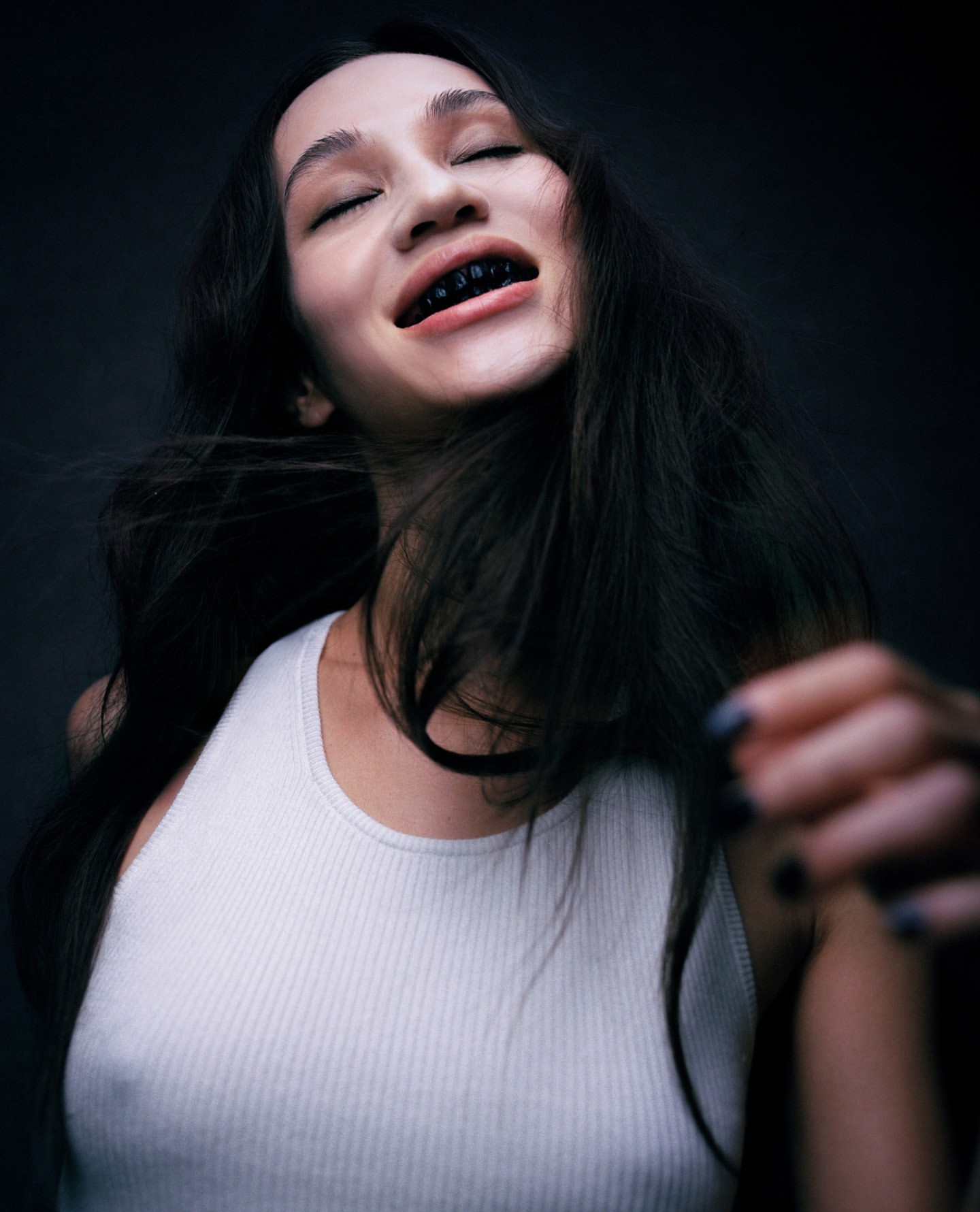 Close-up portrait of a young adult woman with long dark hair, wearing a white tank top, and an upward camera angle.