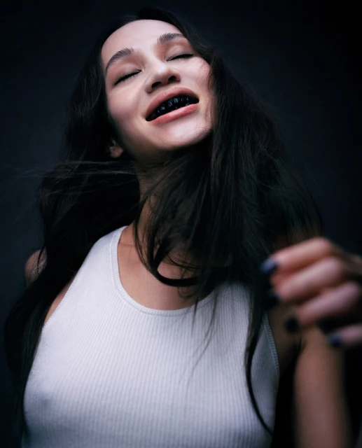 Close-up portrait of a young adult woman with long dark hair, wearing a white tank top, and an upward camera angle.