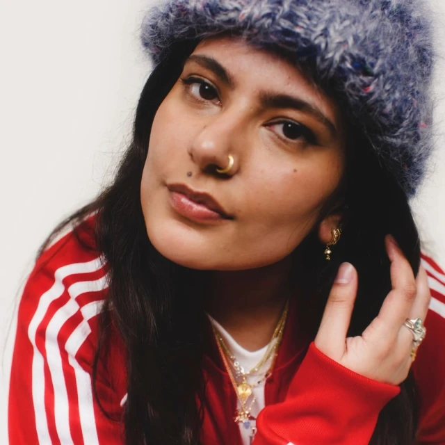 Close-up portrait of an adult woman wearing a knit hat and a red and white track jacket against a white background.