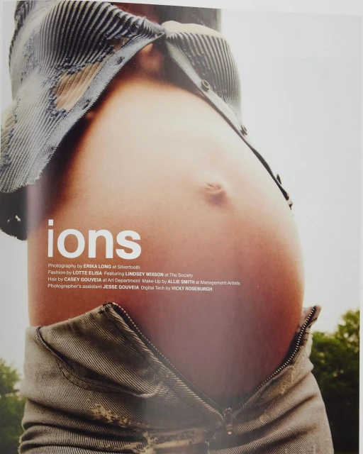 Close-up studio shot of a pregnant adult female showing bare belly with open jeans and shirt against a blurred outdoor background.