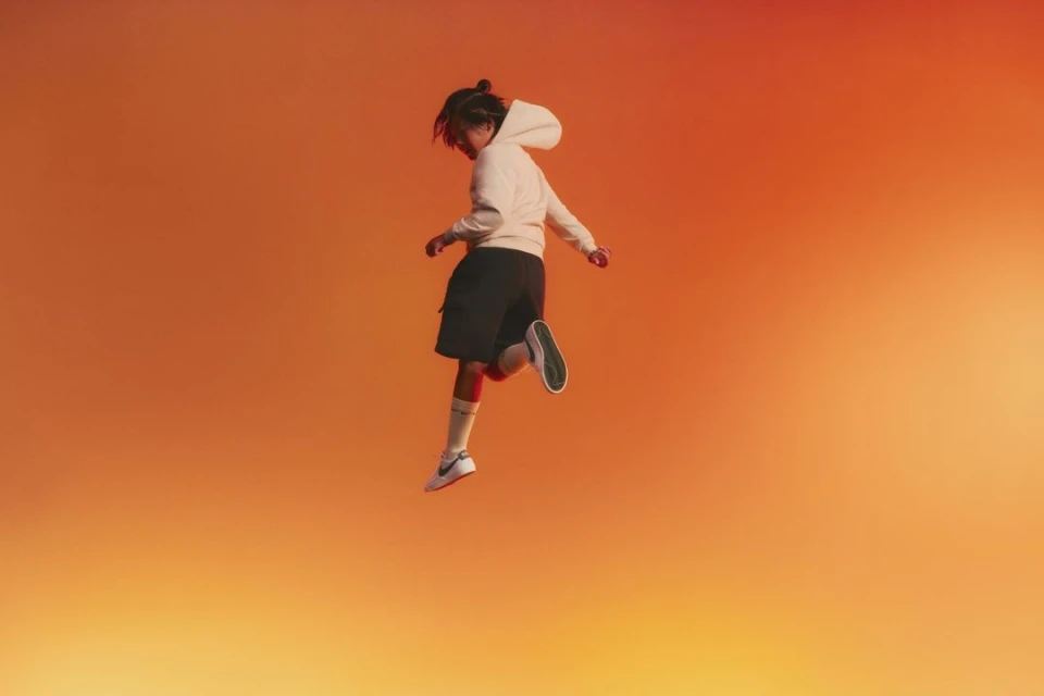 Teenager in mid-air wearing athletic wear on orange gradient background, athletic pose, studio shot, active lifestyle concept.
