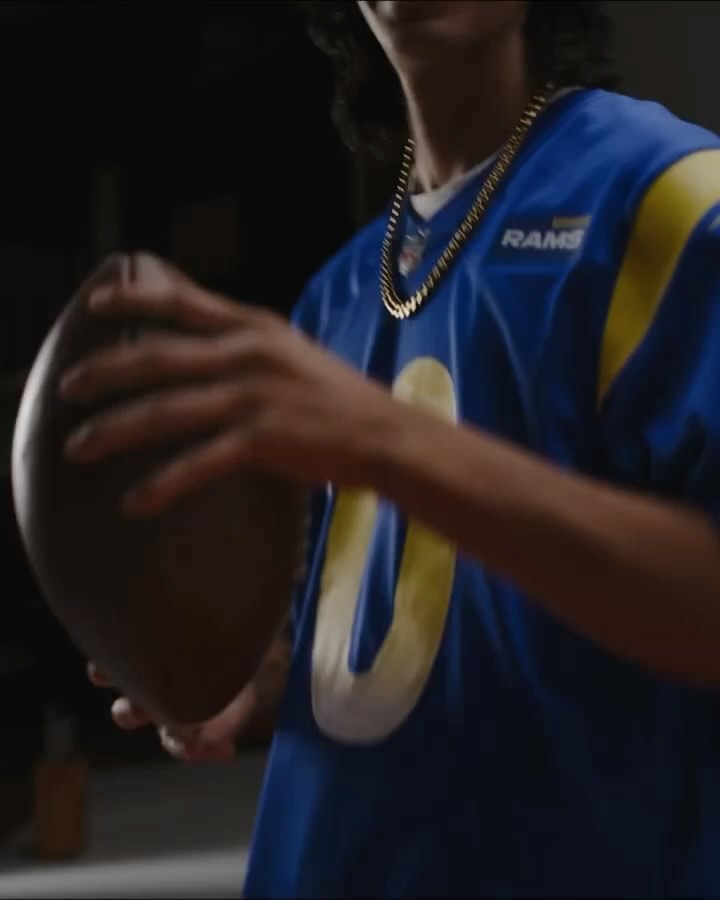 Person in Rams jersey holds a football indoors under warm lighting, showcasing sport and team spirit with a close-up focus.