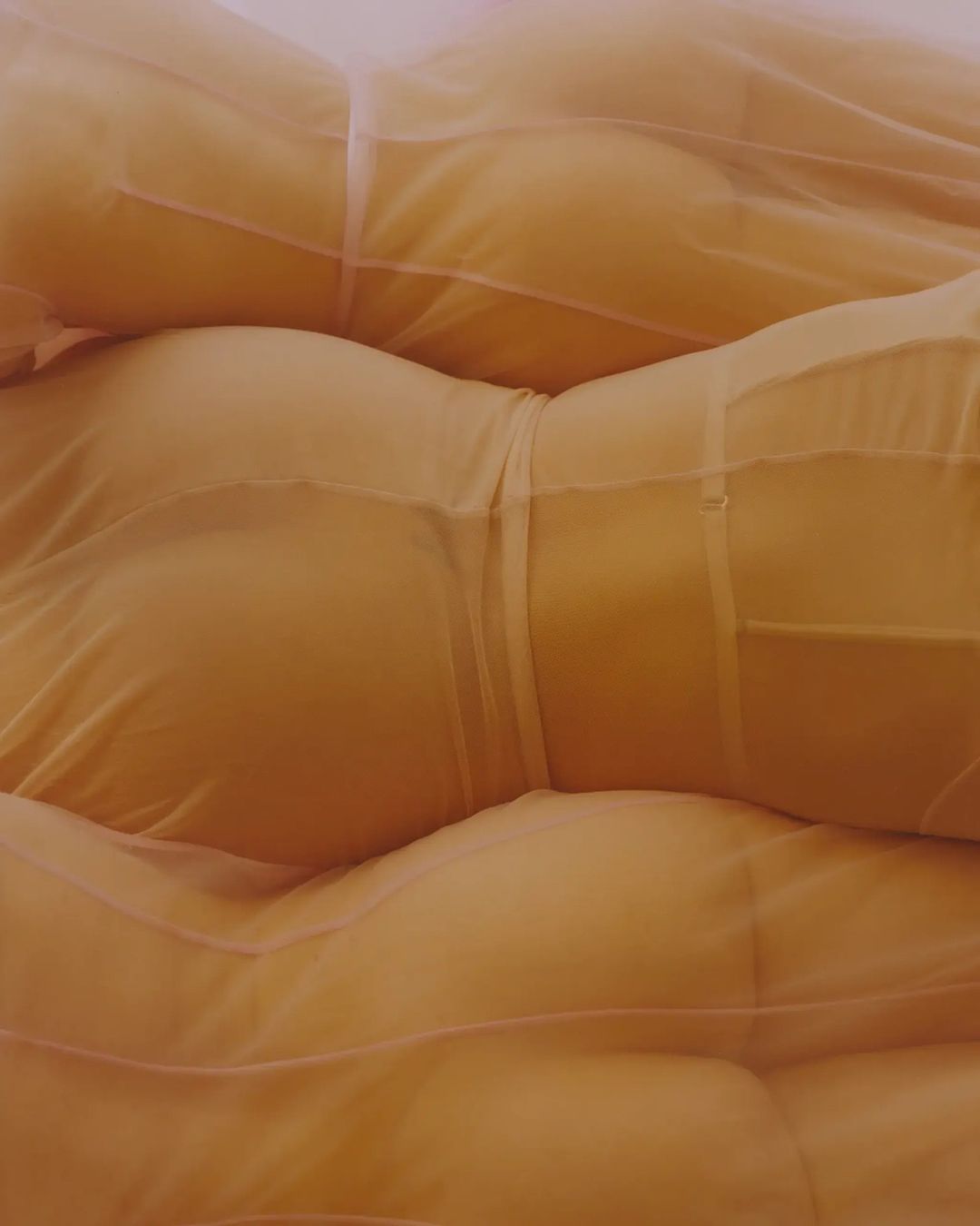 Overlapping images of women's torsos wrapped in a sheer orange fabric, creating an abstract yet sensual visual texture and form.