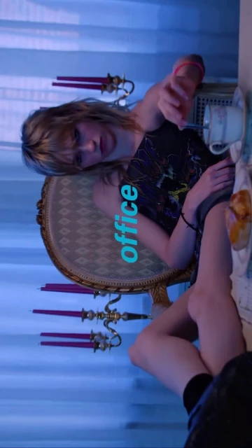Young adult woman at a table with teacups and candles in a domestic indoor setting with soft lighting and a vintage aesthetic.