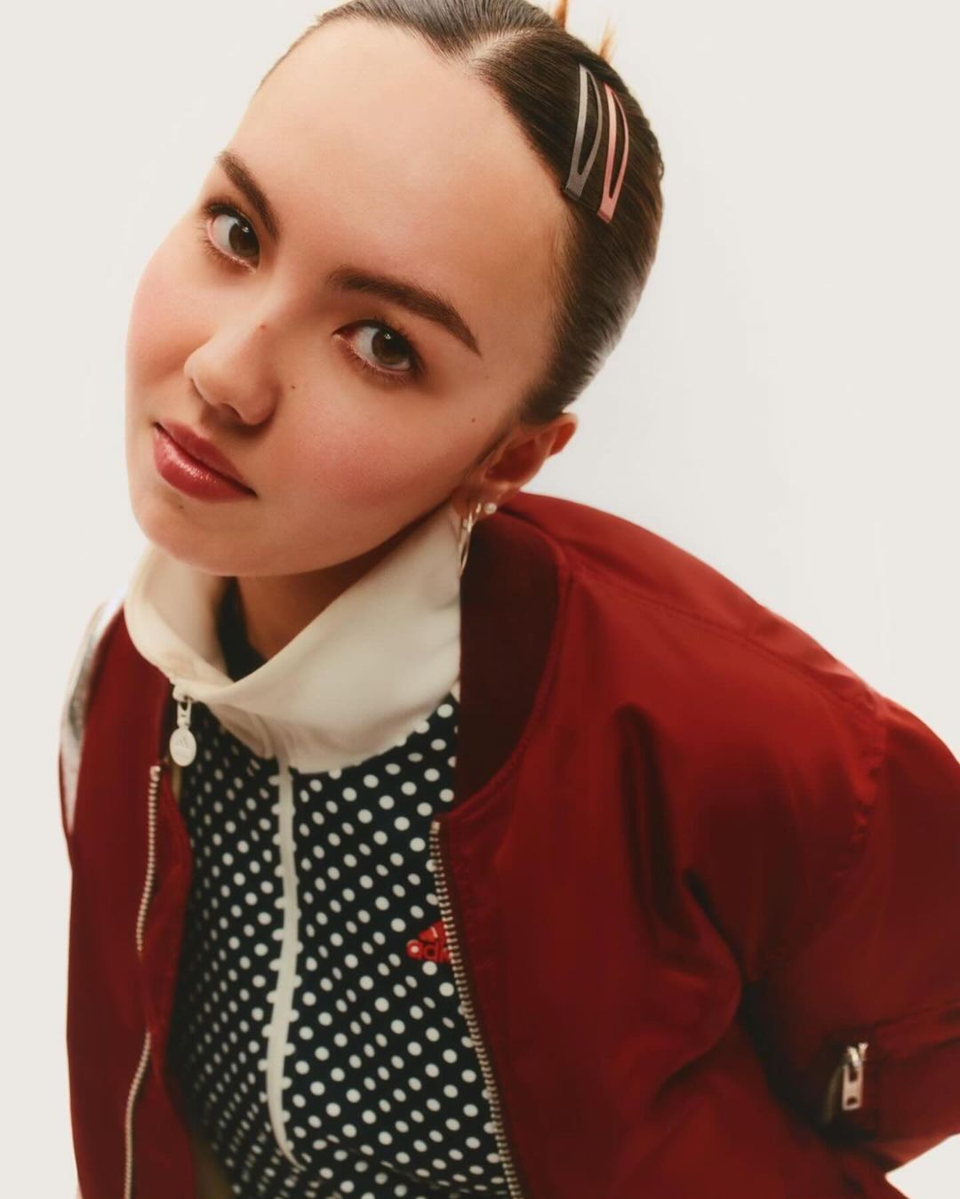 Headshot of a young woman with bobby pins in her hair, wearing a burgundy bomber jacket and a black-and-white polka dot top.