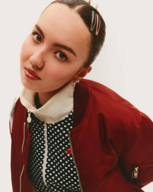 Headshot of a young woman with bobby pins in her hair, wearing a burgundy bomber jacket and a black-and-white polka dot top.