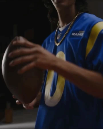 Man wearing a blue football jersey with a gold chain necklace holding an American football