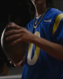Man wearing a blue football jersey with a gold chain necklace holding an American football