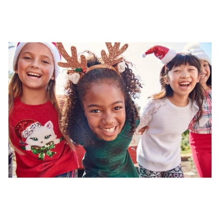 Four laughing girls wearing holiday headbands and sweaters pose outdoors. A joyful group portrait captures the festive spirit of the season.