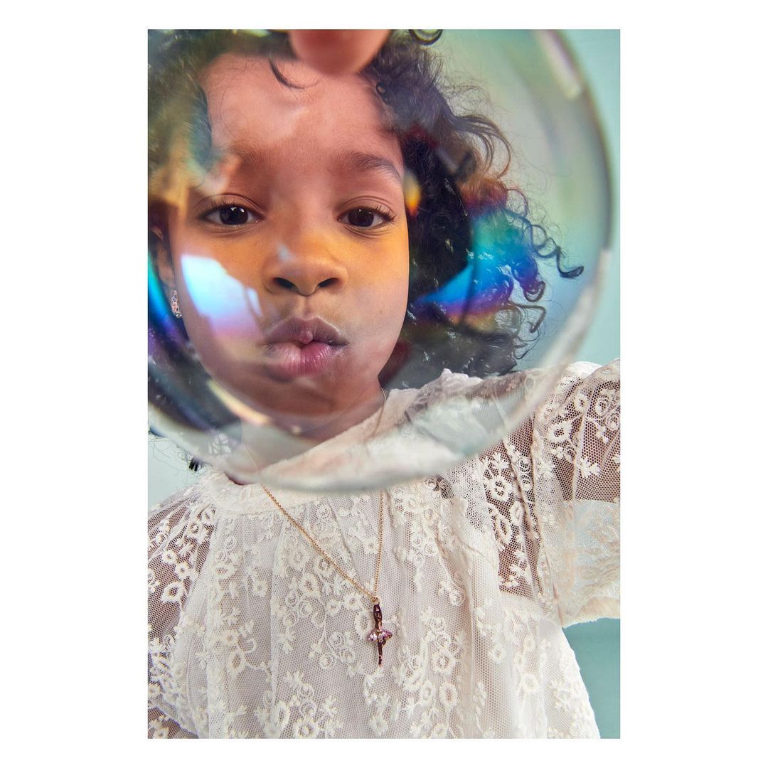 Adorable child in lace top blows iridescent bubble, capturing a moment of innocence and wonder with a dreamy, soft focus.