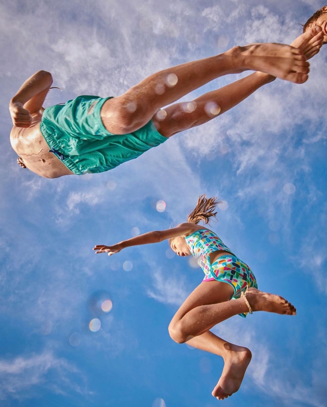 Two children jumping against a bright blue sky with water droplets visible in the air