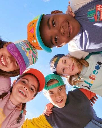 Upward angle capturing smiling children with baseball caps, looking down at the camera against a blue sky backdrop.
