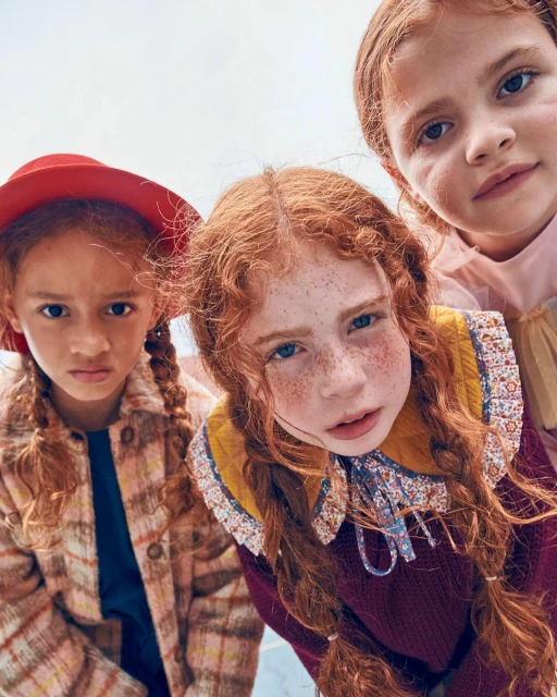 Low-angle portrait of three young red-haired girls in vintage-style clothing. The girls are close together, filling the frame.