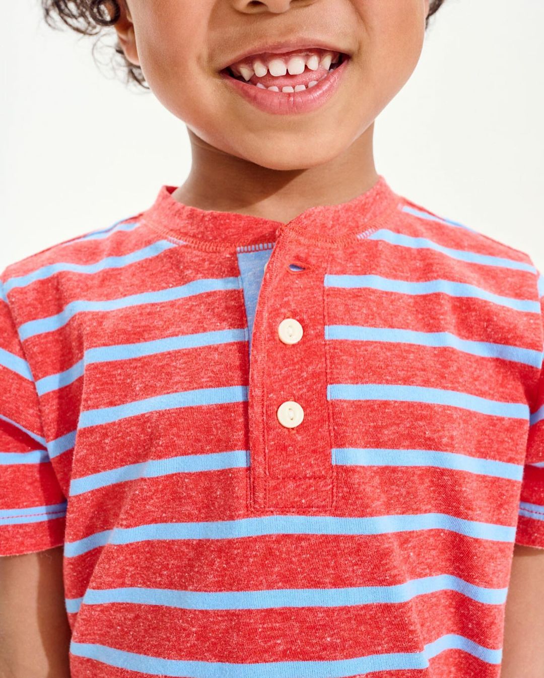 Close-up of a smiling child in a striped orange t-shirt, showcasing their upper body and joyful expression against a bright background.