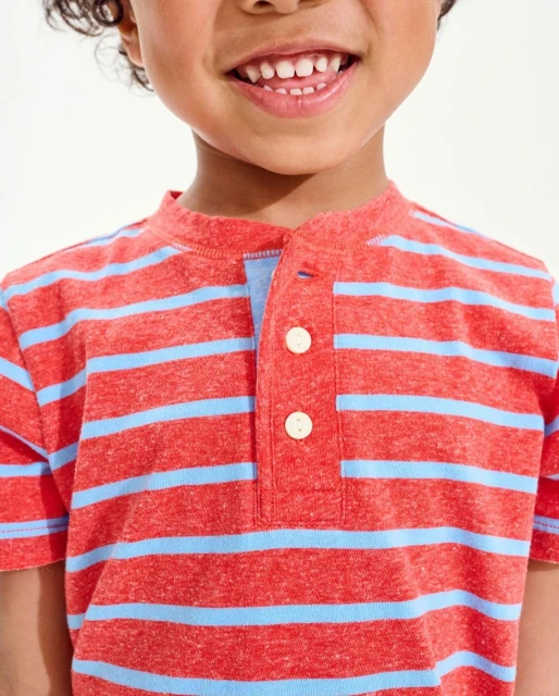 Close-up of a smiling child in a striped orange t-shirt, showcasing their upper body and joyful expression against a bright background.