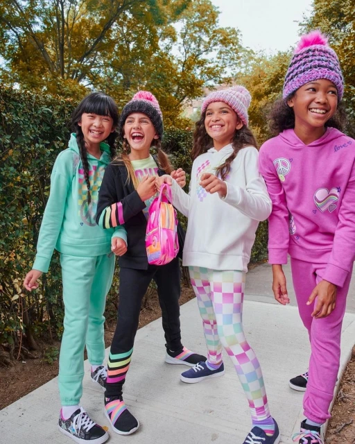 Four smiling girls in brightly colored activewear stand together outdoors with greenery, creating a happy, vibrant, and youthful image.