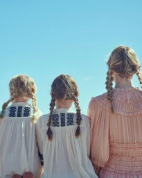 Three female models from behind wearing braided hairstyles against a clear blue sky background