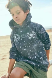 Child wearing dark patterned hoodie and green shorts outdoors against a bright sky background photographed by Erin Foster