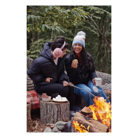 Two women roasting marshmallows over a campfire outdoors wearing winter jackets and hats
