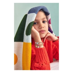 Young girl draped in a colourful patterned knit blanket wearing an orange sweater and beaded heart bracelets, photographed by Erin Foster
