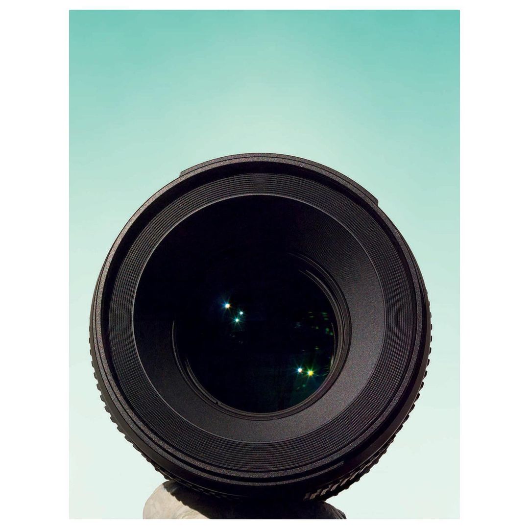 Close-up studio shot of a camera lens against a solid teal background, showcasing its focus and clarity for photography.