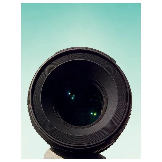 Close-up studio shot of a camera lens against a solid teal background, showcasing its focus and clarity for photography.