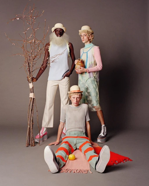 Three fashion models pose indoors in hats and outfits with unique textures, colors, and platform shoes against a plain grey background.