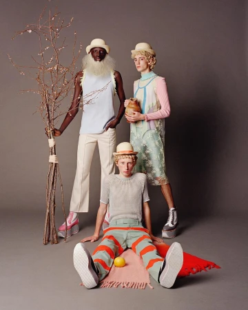 Three fashion models pose indoors in hats and outfits with unique textures, colors, and platform shoes against a plain grey background.