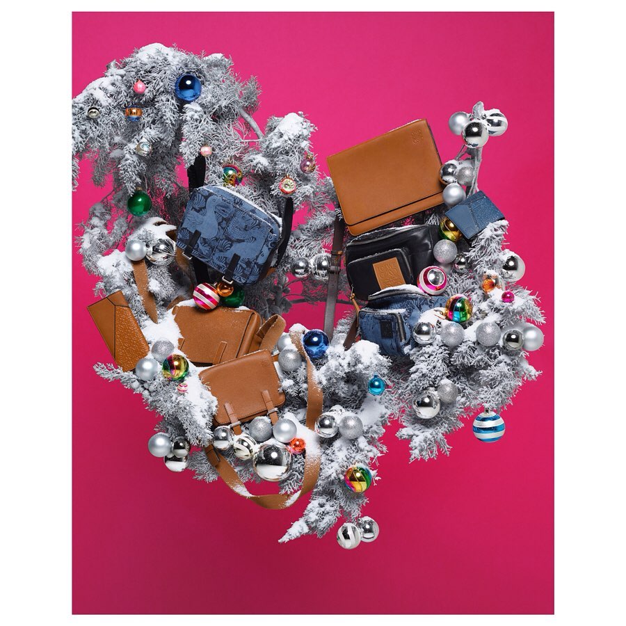 Display of handbags in various styles and materials, arranged on snowy branches decorated with colorful ornaments against a pink backdrop.