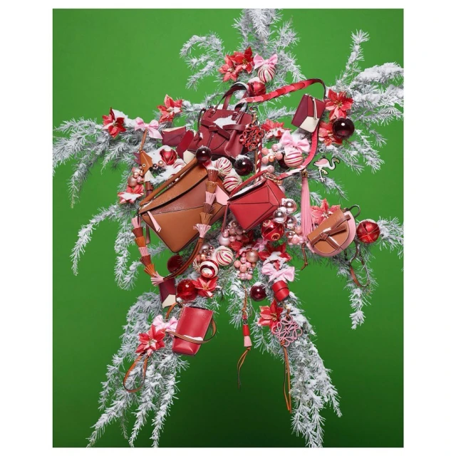 Festive arrangement featuring a variety of small handbags in red and brown hues, nestled among white, snow-covered branches and colorful ornaments.