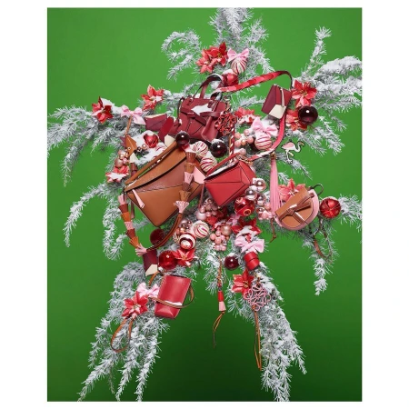 Festive arrangement featuring a variety of small handbags in red and brown hues, nestled among white, snow-covered branches and colorful ornaments.