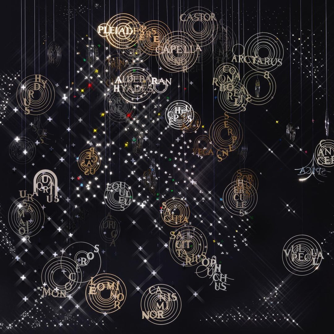 Art installation with celestial star maps, constellation names, and geometric starbursts suspended against a dark night sky background.