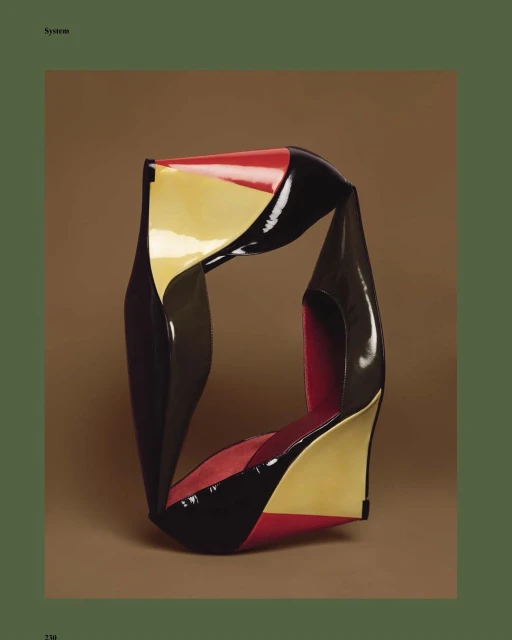 Abstract glossy sculpture in black, red, and yellow against a brown backdrop. Modern art piece with smooth, reflective surfaces.