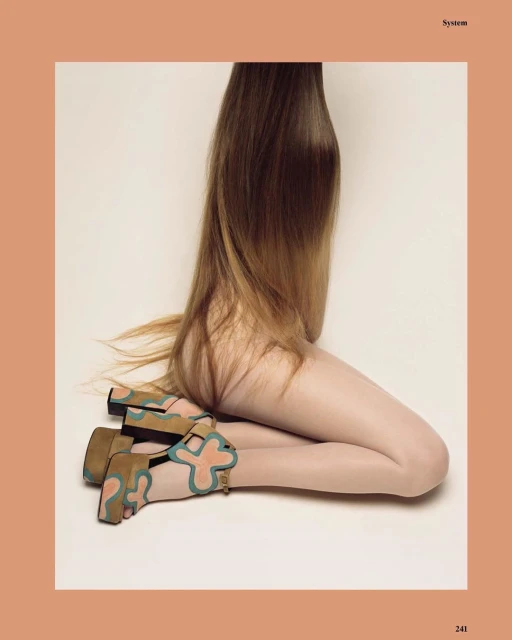 A model with long, blonde hair is kneeling and wearing sandal heels with light orange and teal accents in a studio shot.