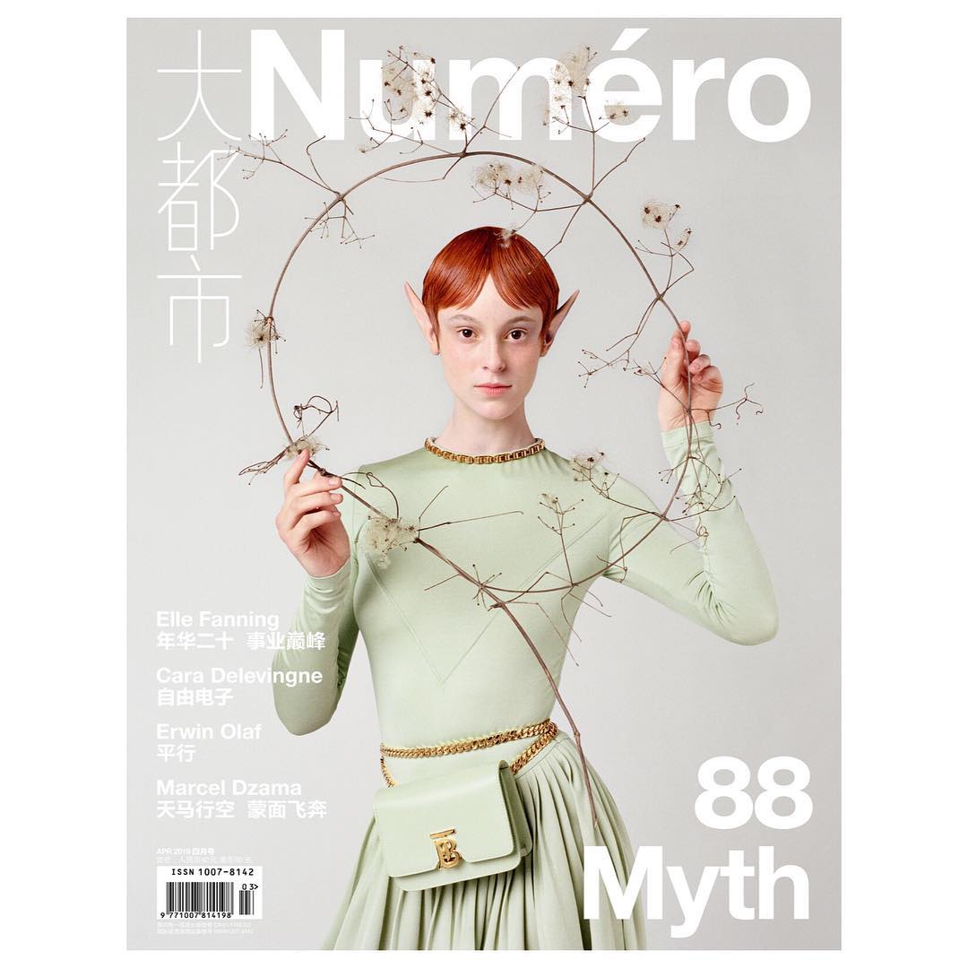 Fashion magazine cover featuring a redhead adult woman in a light green dress and a purse, standing against a grey studio backdrop.
