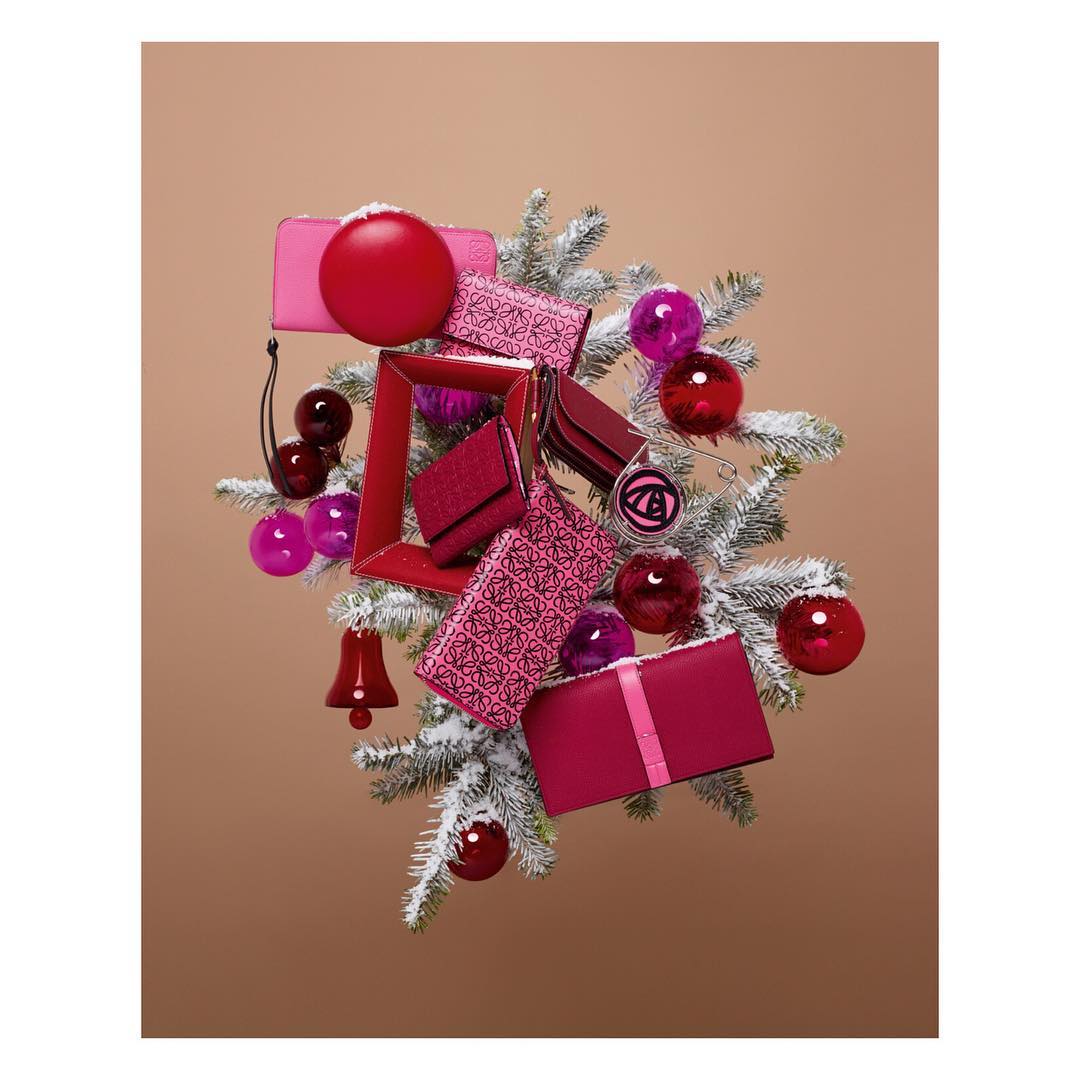 Luxury handbag display with Christmas ornaments on snow-flocked pine branch against a tan backdrop. Festive product presentation.