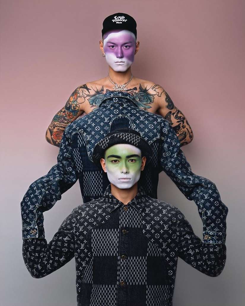 Two stylish men showcase patterned shirts and face paint against a pink background, highlighting fashion and creative makeup.