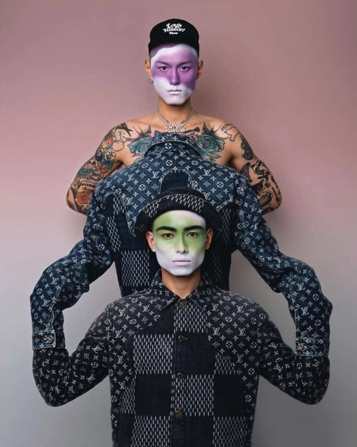 Two stylish men showcase patterned shirts and face paint against a pink background, highlighting fashion and creative makeup.