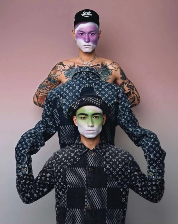 Two stylish men showcase patterned shirts and face paint against a pink background, highlighting fashion and creative makeup.