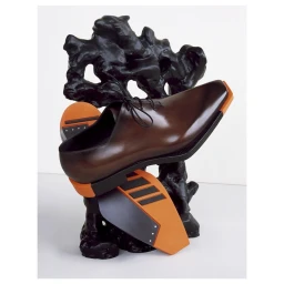 Brown leather dress shoe balanced on a dark organic sculpture against a solid white background