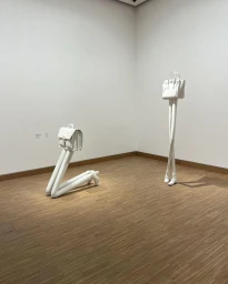 White sculptural installations of handbags with long slender legs standing in a gallery interior with wooden parquet flooring.