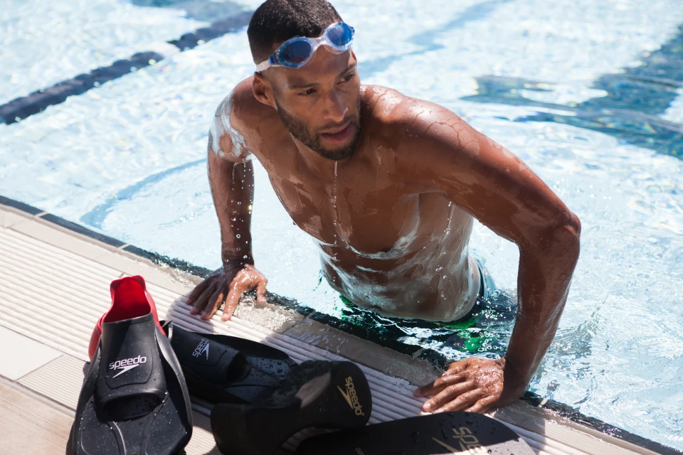 Man emerges from a swimming pool wearing goggles, with swimming fins, on a sunny day, highlighting fitness and aquatic sports.