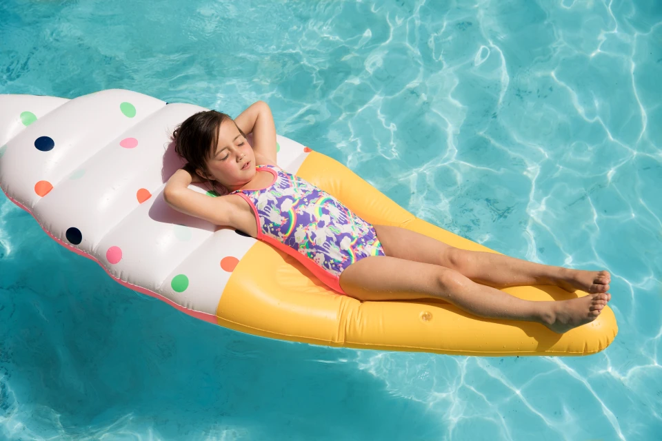 Child relaxing on an ice cream float in a pool. Summertime image of a young girl in a swimsuit cooling off with her eyes closed.