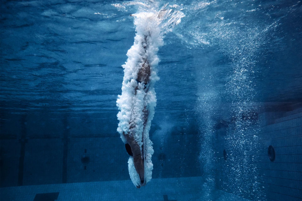 Underwater shot of a swimmer diving into a pool, surrounded by bubbles and blue water, capturing the moment of submersion.