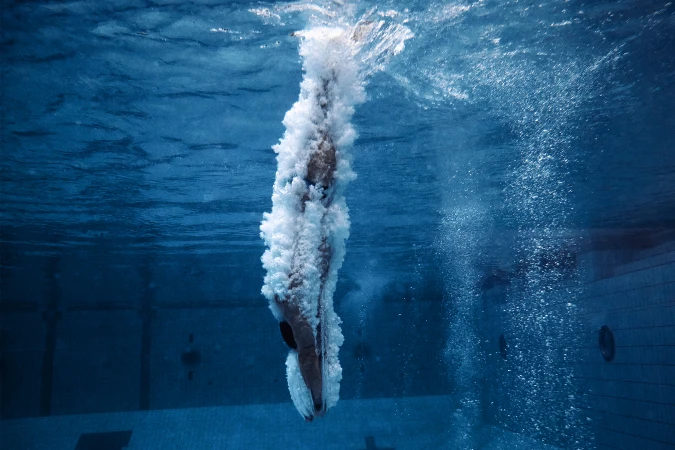 Underwater shot of a swimmer diving into a pool, surrounded by bubbles and blue water, capturing the moment of submersion.