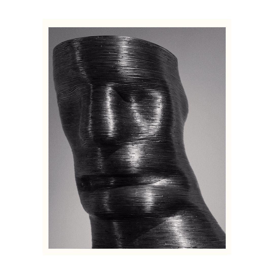Black and white image of a layered, sculptural bust of a human torso and head with a grainy texture against a soft grey background.