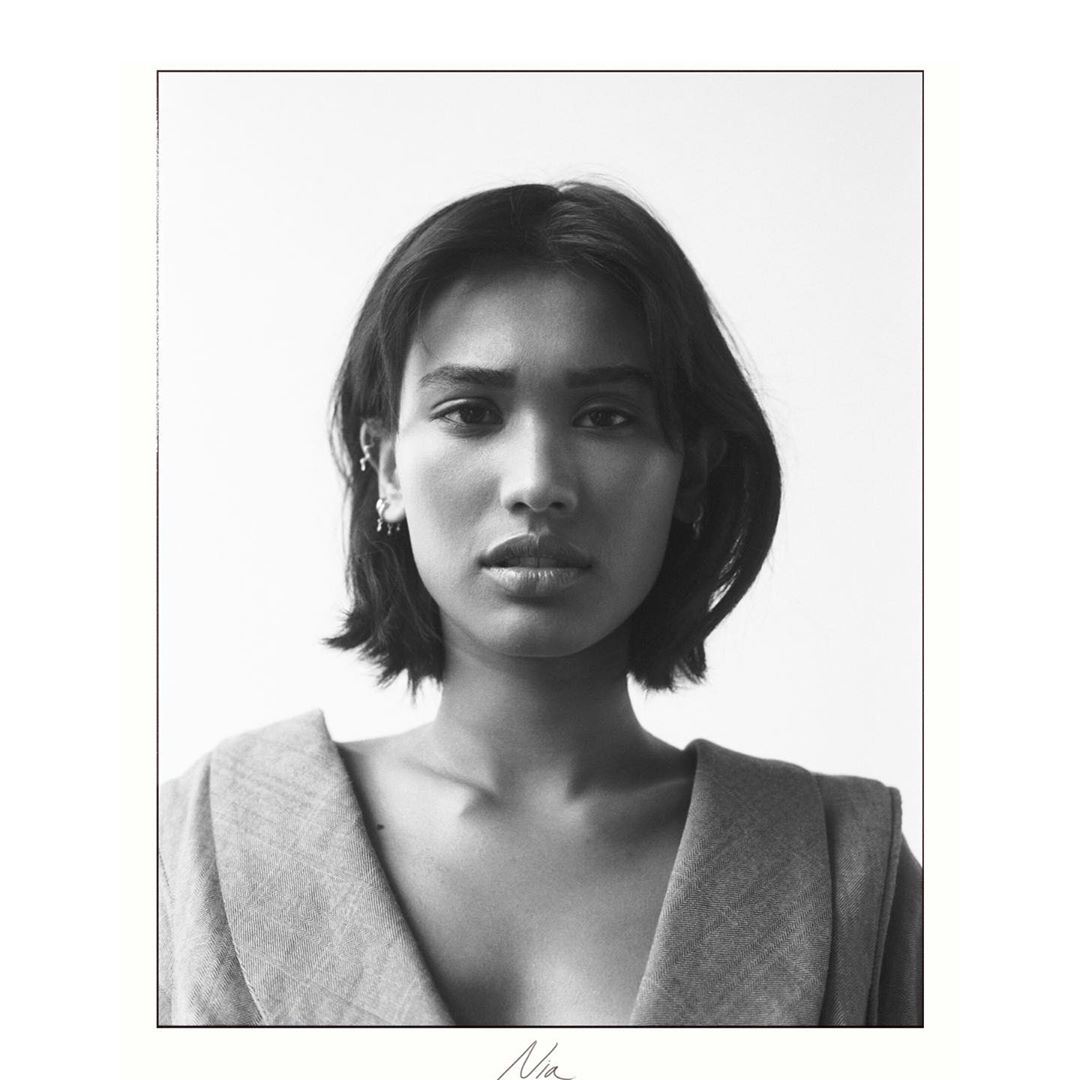 Monochromatic portrait of a woman with short dark hair, wearing a structured jacket against a plain white backdrop in a studio setting.