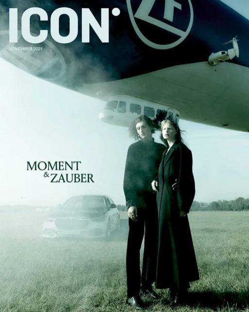 Magazine cover featuring two models standing in a field with a car and blimp, showcasing fashion and automotive elements.