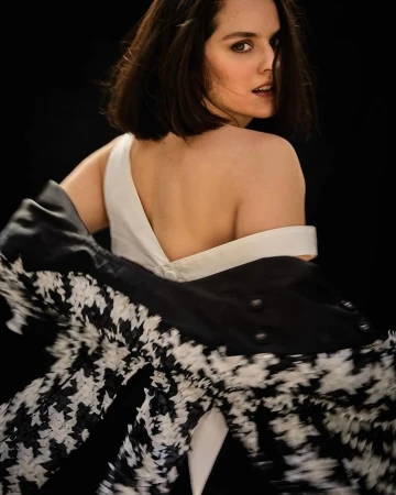 Woman in white top looking back while slipping on a black and white patterned jacket by Esther Haase